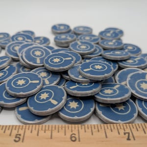 May include: A pile of blue and white game tokens with a star and magnifying glass design.