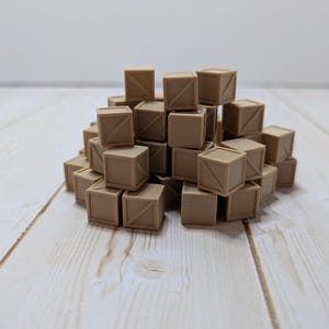May include: A pile of small, tan-colored wooden crates with diagonal bracing on the sides. The crates are stacked on a light-colored wooden surface, creating a textured and visually interesting arrangement. The background is a plain white wall.