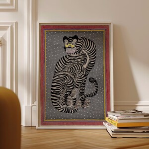 May include: A framed print of a black and white tiger with yellow eyes, sitting on a gray background with white dots. The frame is red with a gold border.