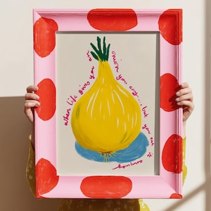 May include: A framed art print featuring a yellow onion illustration with green and blue accents. The pink frame has red polka dots and the text reads "when life gives you onion you cry... but you eat it."