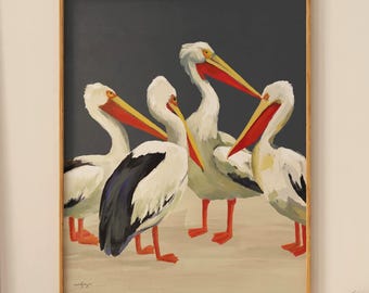 以下が含まれることがあります： ペリカンのグループを描いた額入りのアートワーク。ペリカンは白い羽、黒い翼の模様、明るいオレンジ色のくちばしと足を持っています。背景は濃い灰色で、ペリカンは明るいベージュの表面に立っています。