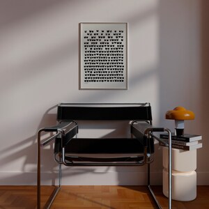 Peut inclure: Un fauteuil en cuir noir avec un cadre chrom&eacute; est plac&eacute; devant un mur blanc avec une impression noir et blanc encadr&eacute;e. Une petite table d'appoint avec une lampe ronde orange et trois livres empil&eacute;s sur le dessus se trouve &agrave; droite du fauteuil.