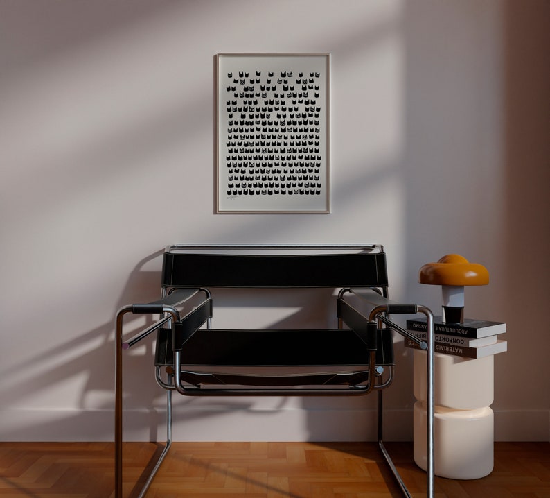 Peut inclure: Un fauteuil en cuir noir avec un cadre chrom&eacute; est plac&eacute; devant un mur blanc avec une impression noir et blanc encadr&eacute;e. Une petite table d'appoint avec une lampe ronde orange et trois livres empil&eacute;s sur le dessus se trouve &agrave; droite du fauteuil.