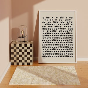 Peut inclure: Une impression encadr&eacute;e blanche avec un motif noir et blanc de visages de chats. L'impression est accroch&eacute;e &agrave; un mur rose p&acirc;le au-dessus d'une table d'appoint &agrave; carreaux noirs et blancs avec une lampe noire sur le dessus.