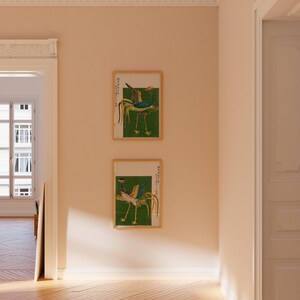 May include: Two framed prints of traditional Chinese artwork depicting a bird with a long tail and colorful feathers on a green background. The prints are in wooden frames and are hanging on a light beige wall.