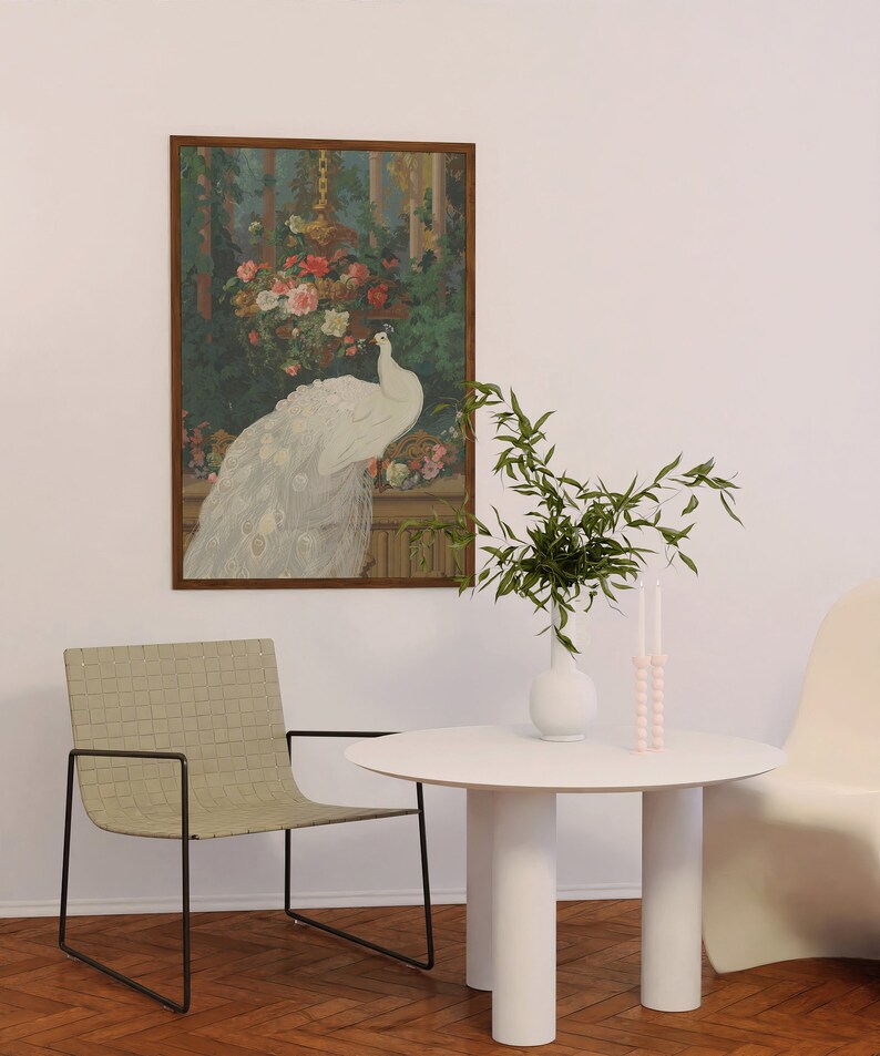 May include: A framed artwork depicts a white peacock with its tail feathers displayed, set against a backdrop of flowers and foliage. A white table with three cylindrical legs, a woven chair, and a vase with greenery and candles complete the scene.