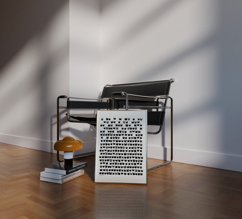 Peut inclure: Une impression graphique noir et blanc dans un cadre argent&eacute; est accroch&eacute;e au mur au-dessus d'une chaise en m&eacute;tal noir avec un coussin noir. Une petite lampe brune est pos&eacute;e sur une pile de livres au sol.