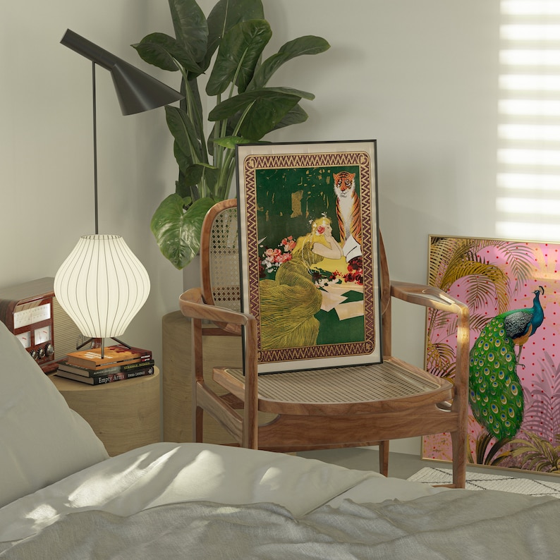 May include: A wooden chair with a woven cane seat and back, featuring a framed print of a woman and a tiger. The print has a gold border and a green background. A second framed print of a peacock with a pink background is on the wall behind the chair.