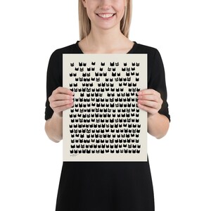 Peut inclure: Une affiche blanche avec un motif noir et blanc de visages de chats. L'affiche est tenue par une personne.