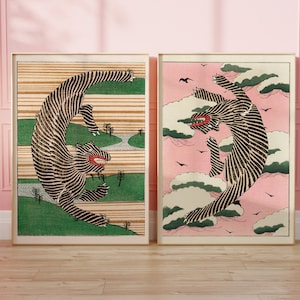 May include: Two framed prints of black and white stylized illustrations of a tiger. One print features a tiger leaping through the air against a pink and white cloudy sky. The other print features a tiger leaping through the air against a green and brown landscape.