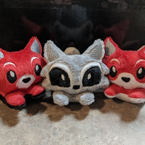 May include: Three plush toys shaped like foxes. One is red, one is gray, and one is red with white accents. The toys have embroidered eyes and noses.