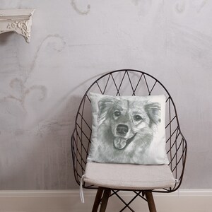 May include: A white throw pillow with a black and white sketch of a dog's face. The dog is smiling with its tongue sticking out. The pillow is sitting on a black metal chair with a white cushion.