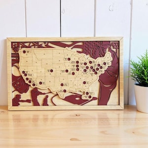 May include: Wooden United States map with a natural wood finish and a burgundy-colored border and accents. The map features state outlines, city markers, and baseball-themed imagery. The map is framed and ready to hang.