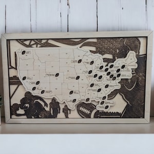 May include: A wooden map of the United States with a brown frame. The map is decorated with footballs and silhouettes of football players. The map is on a white shelf with a white wall in the background.