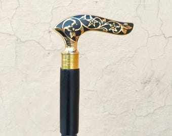 Könnte beinhalten: Ein Gehstock mit schwarzem Schaft und gebogenem Griff. Der Griff besteht aus schwarzem Material mit goldfarbenen floralen Gravuren. Ein goldfarbener Metallring verbindet den Griff mit dem Schaft, der eine glatte Oberfläche aufweist.