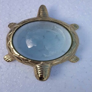 May include: A gold-colored turtle-shaped magnifying glass with a clear glass lens. The turtle has a detailed shell design.