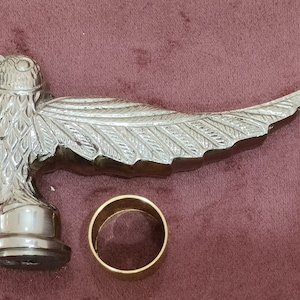 May include: Silver-toned metal bird-shaped walking stick handle with a detailed design. The handle is attached to a gold-colored metal ring.