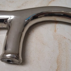 May include: A polished chrome walking stick handle with a unique curved design. The handle has a smooth, shiny finish and a hole at the bottom for attaching the stick.