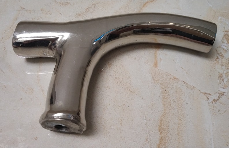 May include: A polished chrome walking stick handle with a unique curved design. The handle has a smooth, shiny finish and a hole at the bottom for attaching the stick.