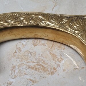 May include: A gold-colored metal cane handle with an intricate floral design.