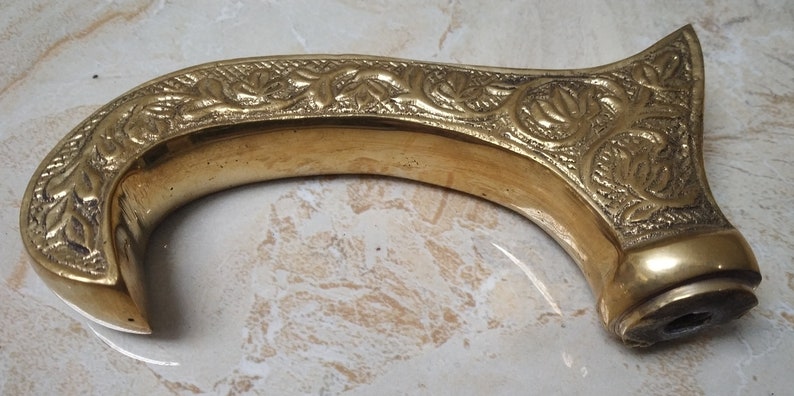 May include: A gold-colored metal cane handle with an intricate floral design.