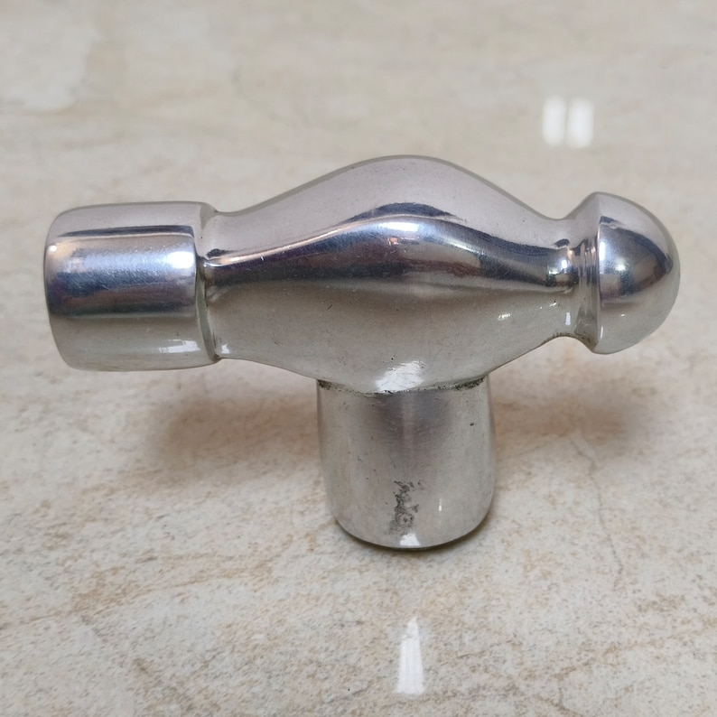 May include: A silver-coloured hammer with a rounded head and a T-shaped handle.