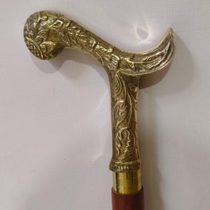 Puede incluir: Un bastón de paseo dorado con un diseño floral ornamentado. El mango es curvo y tiene un patrón floral detallado. El bastón está hecho de metal y tiene un eje de madera.