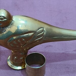 May include: A gold-colored metal bird-shaped walking stick handle with intricate details. The handle is attached to a round metal base.