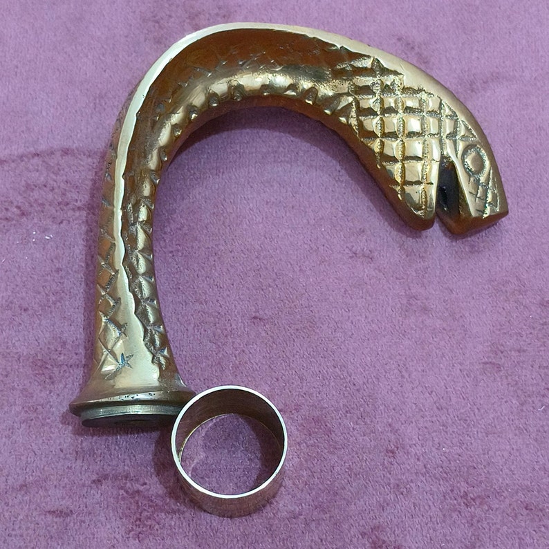 May include: A gold-colored metal cane handle shaped like a snake's head with a textured surface. The handle is attached to a round metal ring.