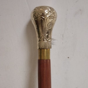 May include: A wooden walking stick with a brass handle. The handle is decorated with a floral design.
