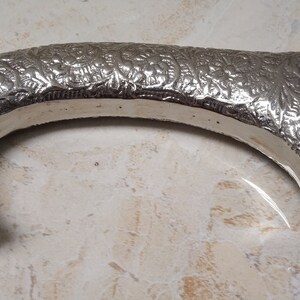 May include: Silver-toned walking stick handle with an ornate floral design. The handle is curved and has a round base.