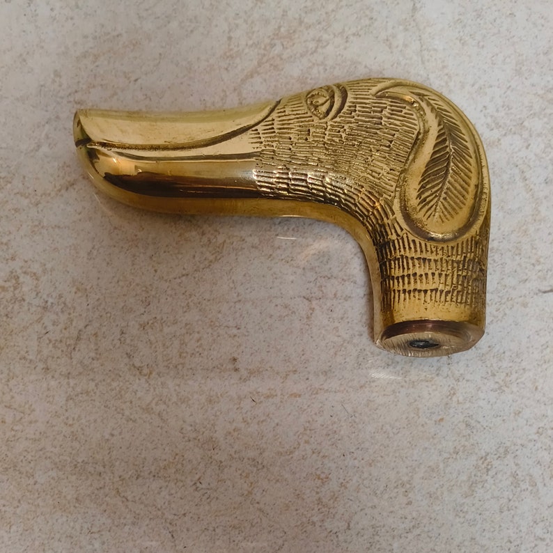 May include: A gold-coloured metal cane handle shaped like a duck's head.