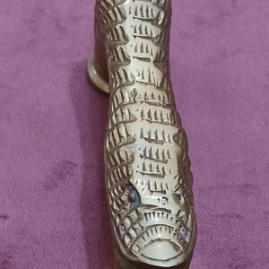 May include: A gold-colored metal door handle shaped like a snake with a textured surface.