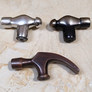 Puede incluir: Tres tiradores de puerta con forma de martillo. Uno es plateado, otro es negro y otro es marrón.