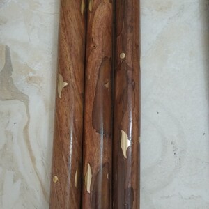 Op de afbeelding: Drie cilindrische houten wandelstoksegmenten met een gepolijste bruine nerf en ingelegde koperen accenten in blad- en puntvormen. De segmenten bevatten metalen schroefverbindingen aan de uiteinden en een zwarte rubberen dop aan de onderkant.