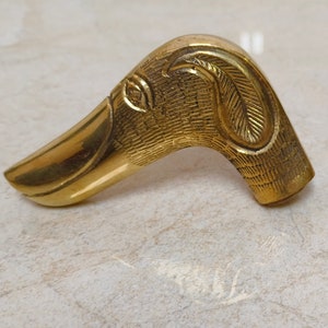 May include: A gold-coloured metal duck head walking stick handle. The handle is detailed with a textured surface and a carved feather design.