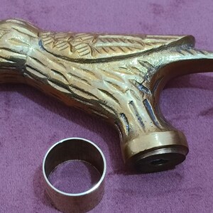 May include: A gold-colored metal bird-shaped cane handle with a decorative design. The handle has a round base with a small hole in the center. A silver-colored metal ring is also included.