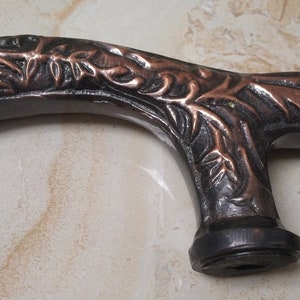 May include: A dark brown and copper colored walking stick handle with an intricate floral design.