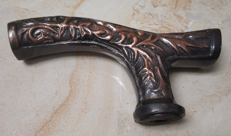 May include: A dark brown and copper colored walking stick handle with an intricate floral design.