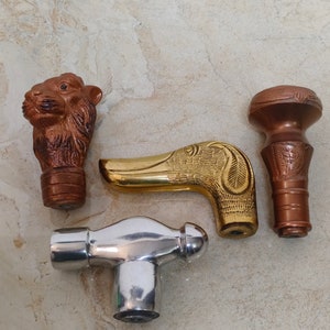 May include: Four different cane or walking stick handles. One is a brown animal head, one is a gold dog head, one is a silver hammer, and one is a brown and gold ornate design.