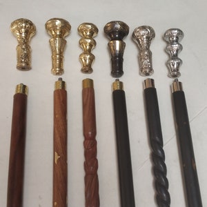 May include: Eight wooden walking sticks with different decorative metal tops. The tops are in gold, silver, and black metal. The sticks are all approximately 91 cm long.