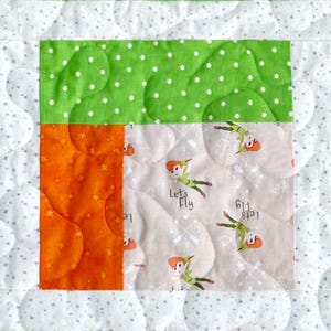 May include: A quilted fabric block featuring a white background with small gray stars, a bright green section with white polka dots, a solid orange section with star patterns, and a light beige section with Peter Pan and the text Let's Fly.
