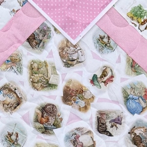 Puede incluir: Una colcha acolchada para bebé con ilustraciones de personajes de cuentos. La colcha tiene un fondo blanco con detalles en rosa y un estampado de lunares rosas. Las ilustraciones representan animales en varias escenas.