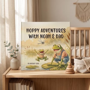 May include: A children's book titled "Hoppy Adventures With Noah & Dad" features a watercolor illustration of two frogs and a dragonfly. The cover art is set against a soft, neutral background with the author's name, "by Nested Sage."