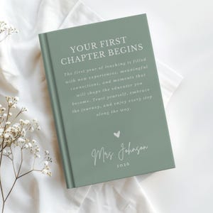 May include: A sage green hardcover book with white text that reads: YOUR FIRST CHAPTER BEGINS. The first year of teaching is filled with new experiences, meaningful connections, and moments that will shape the educator you become. Mrs. Johnson 2026.