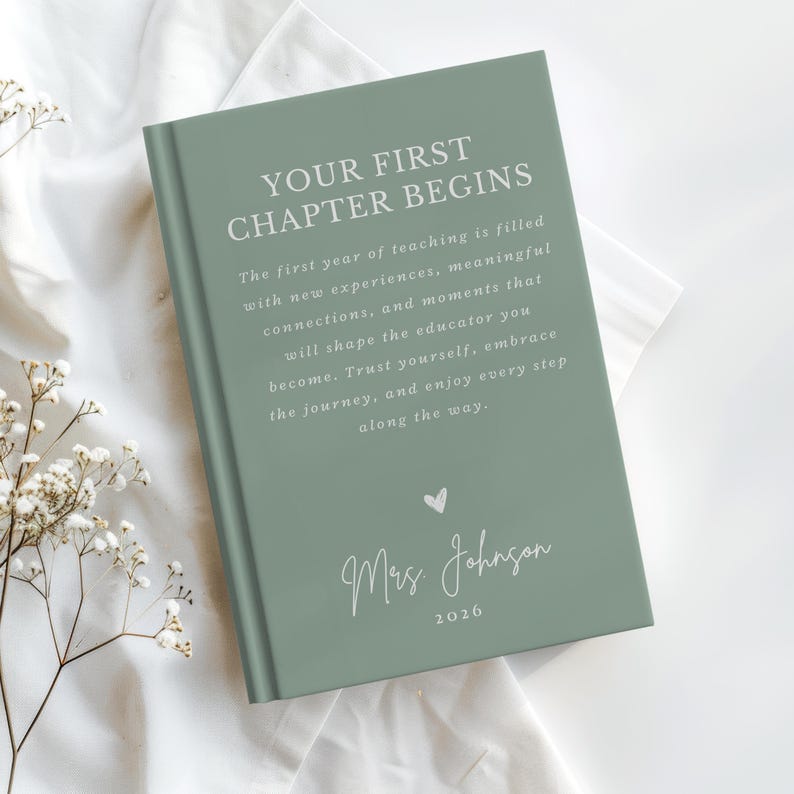May include: A sage green hardcover book with white text that reads: YOUR FIRST CHAPTER BEGINS. The first year of teaching is filled with new experiences, meaningful connections, and moments that will shape the educator you become. Mrs. Johnson 2026.