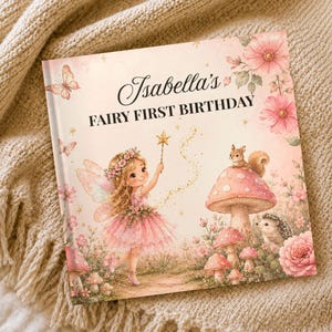May include: A square hardcover book titled Isabella's FAIRY FIRST BIRTHDAY, featuring a pink illustration of a fairy with wings, a wand, a squirrel on a mushroom, a hedgehog, butterflies, and flowers on a soft pastel background.