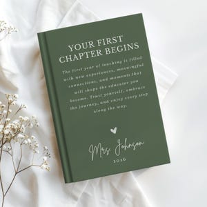 May include: A dark green hardcover book with white text that reads: YOUR FIRST CHAPTER BEGINS. The first year of teaching is filled with new experiences, meaningful connections, and moments that will shape the educator you become. Mrs. Johnson 2026.