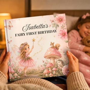 May include: A hardcover book titled Isabella's FAIRY FIRST BIRTHDAY featuring a whimsical illustration of a fairy with wings, a squirrel on a mushroom, a hedgehog, and pink flowers on a soft pastel background with gold sparkles.
