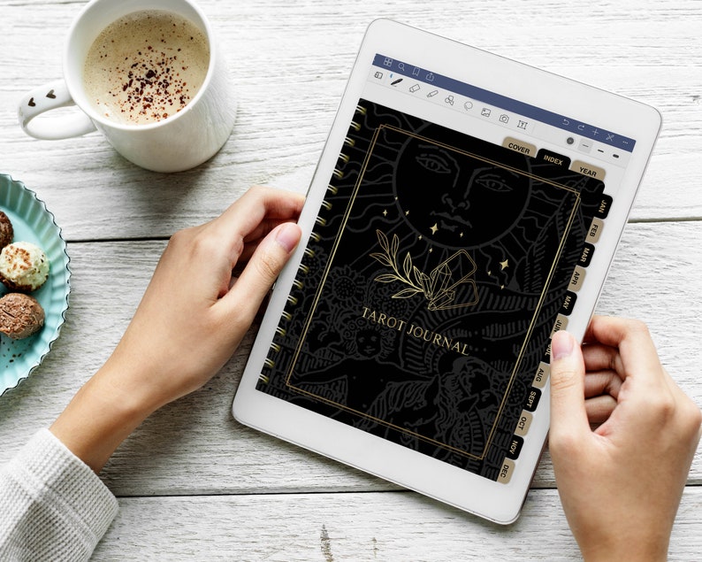 May include: A black and gold tarot journal with a sun and moon design on the cover. The journal has tabs for each month of the year.